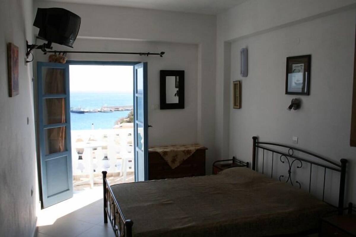 A bedroom with a bed, a view of the sea through an open door, and a balcony with white railings.