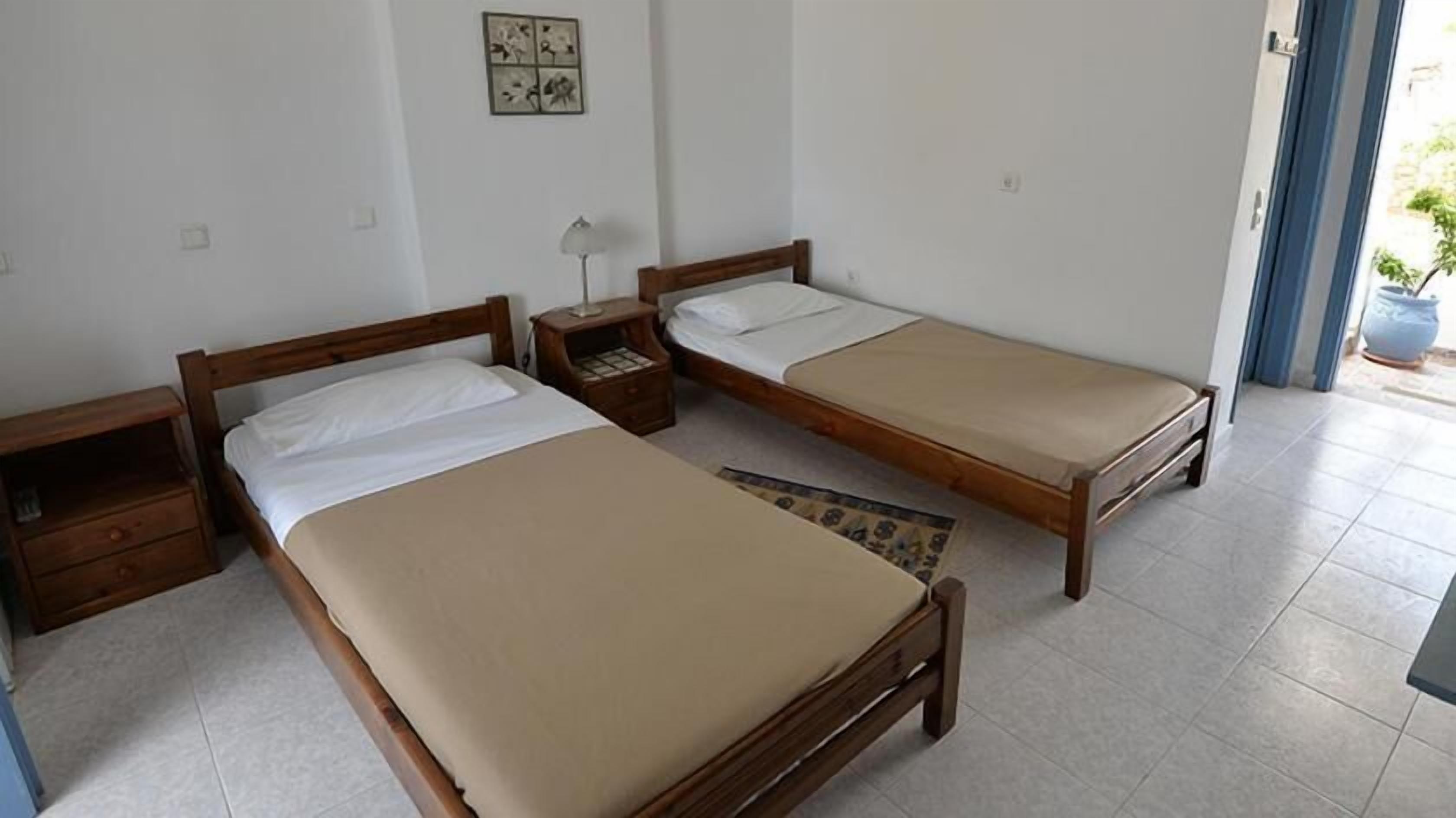 A room with two wooden beds, a nightstand, a small table, and a wall-mounted artwork.