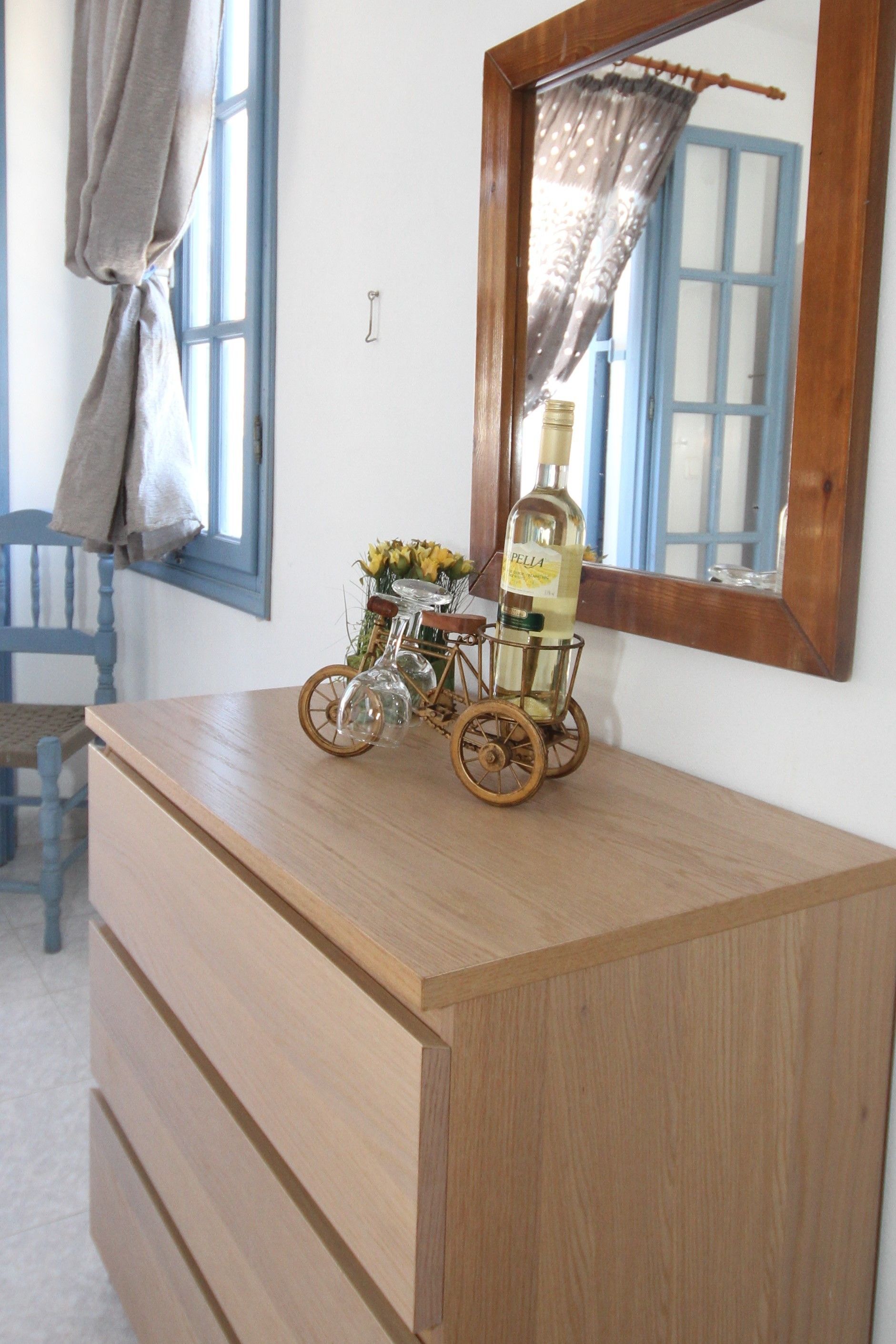 A wooden dresser with a mirror above it, a bicycle-shaped bottle holder with a bottle, and a chair in the background.