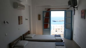 Een kamer met twee eenpersoonsbedden, een airconditioningapparaat, een televisie en uitzicht op de zee door een open deur.