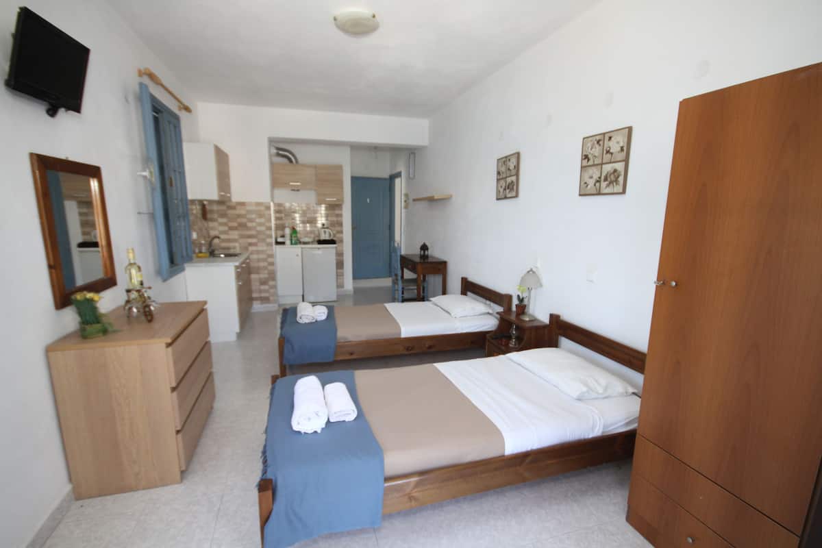 A hotel room with two beds, a wooden wardrobe, a desk with a mirror, and a bathroom visible through an open door.