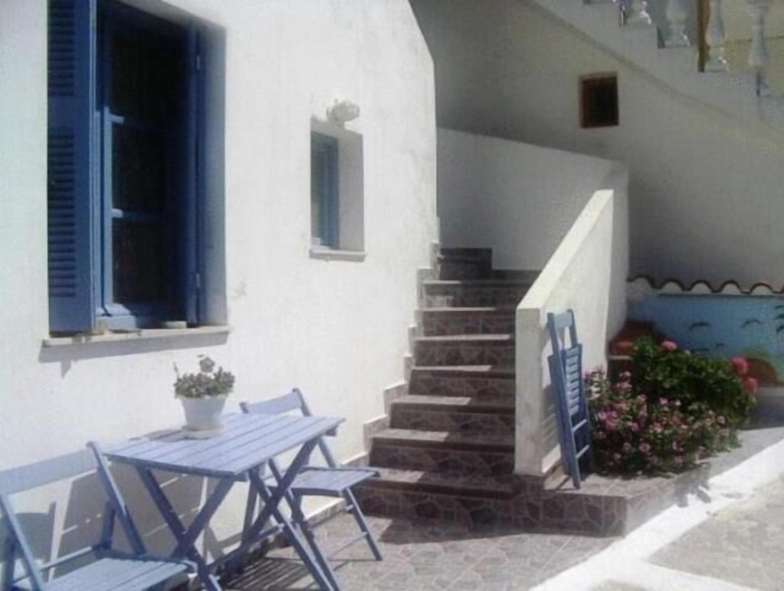 A white building with blue shutters, a small table with chairs, and a staircase leading to an upper floor.
