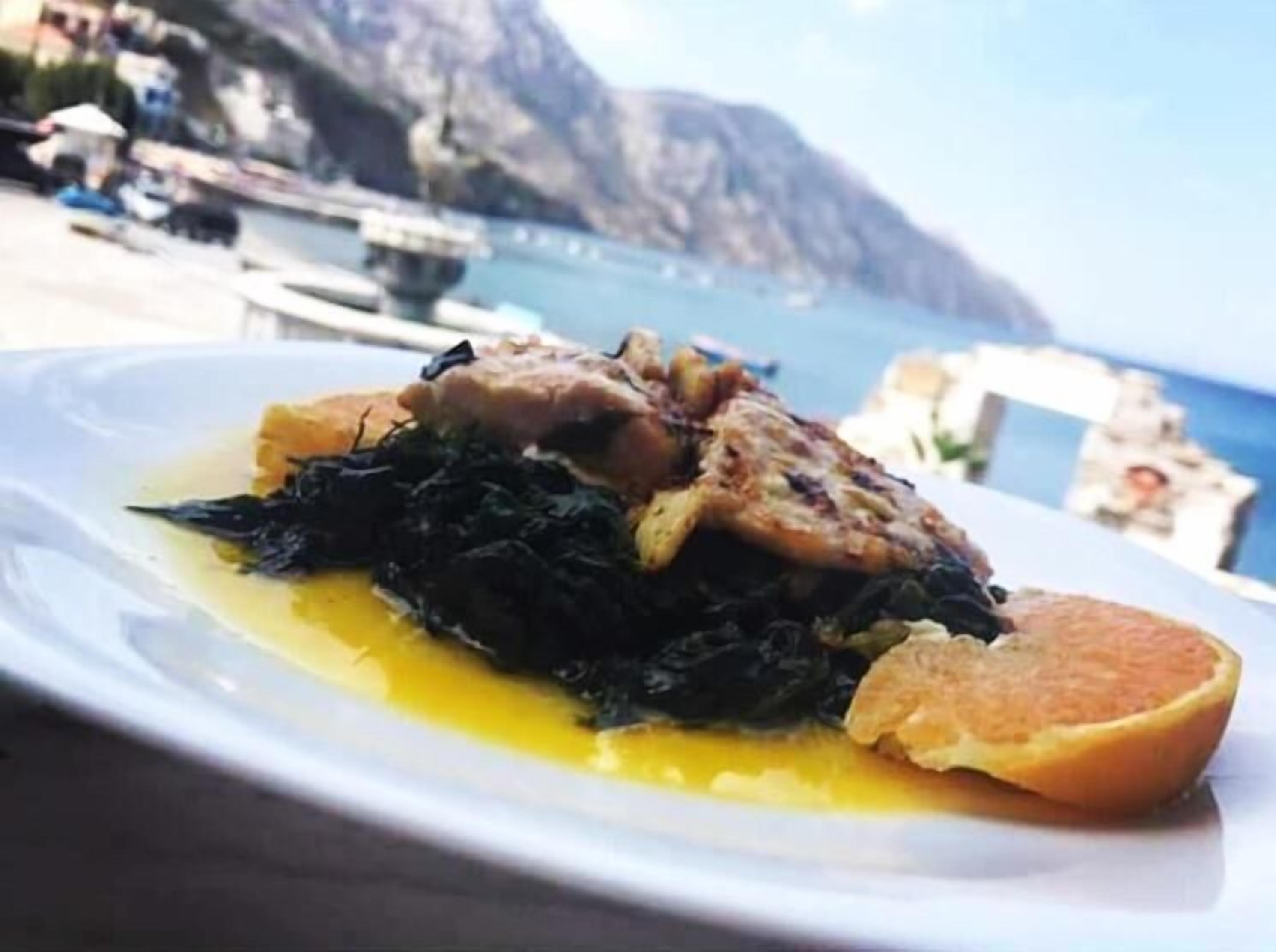 A plate of food with greens, meat, and a slice of orange on a white plate.