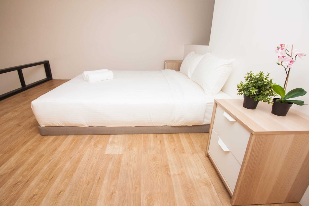 A neatly made bed with white linens, a wooden nightstand with a potted plant, and a wooden dresser with drawers.