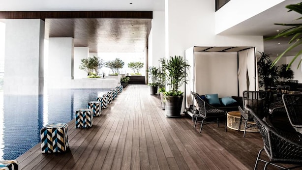 Un espace piscine intérieur moderne, doté d’un plancher en bois, de chaises longues et de plantes en pot.