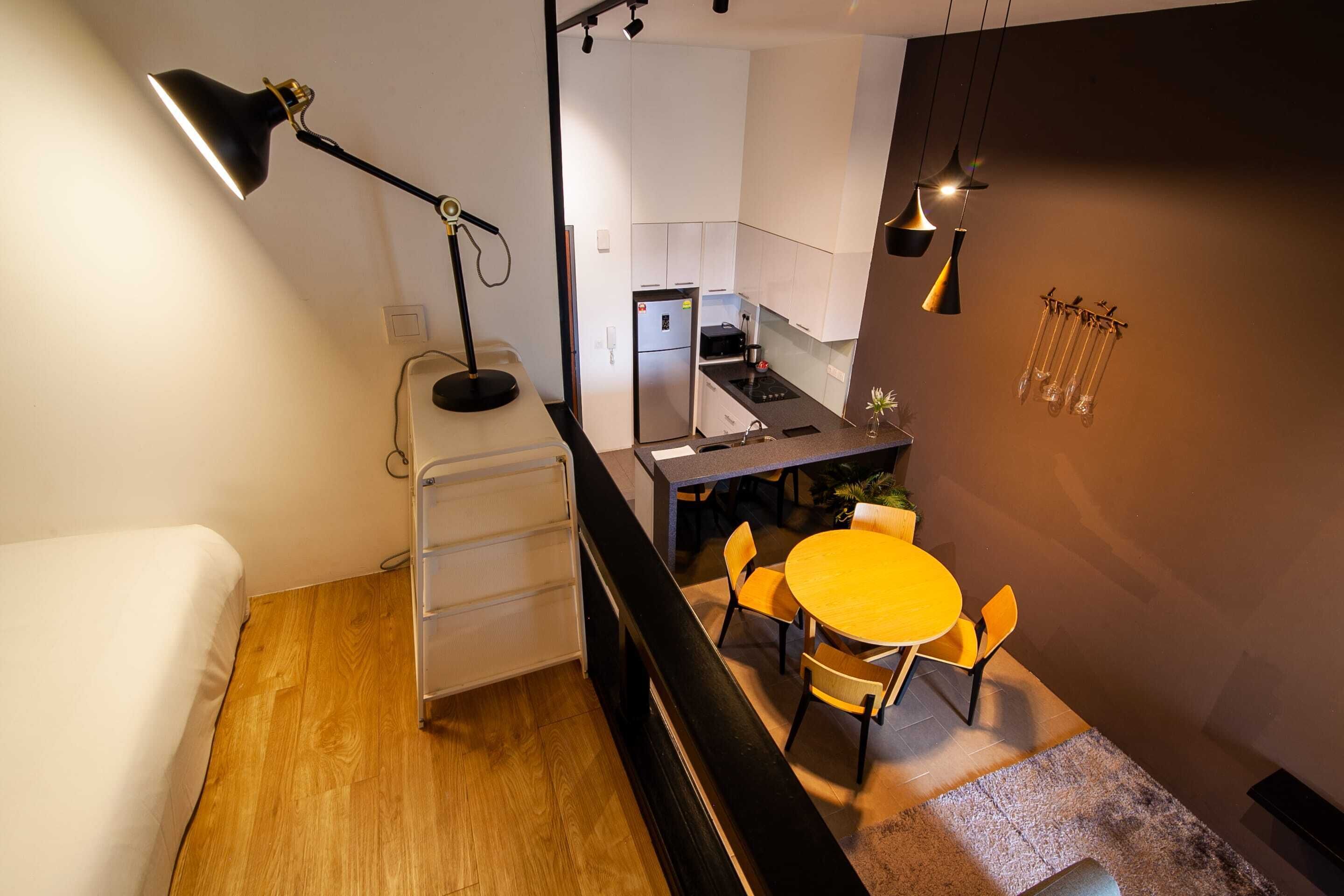 Een compacte keuken met moderne apparaten, een eethoek met een ronde tafel en stoelen, en een bed met een houten vloer.