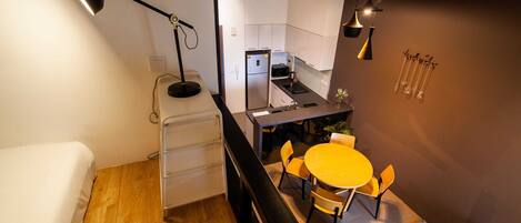 Een compacte keuken met moderne apparaten, een eethoek met een ronde tafel en stoelen, en een bed met een houten vloer.