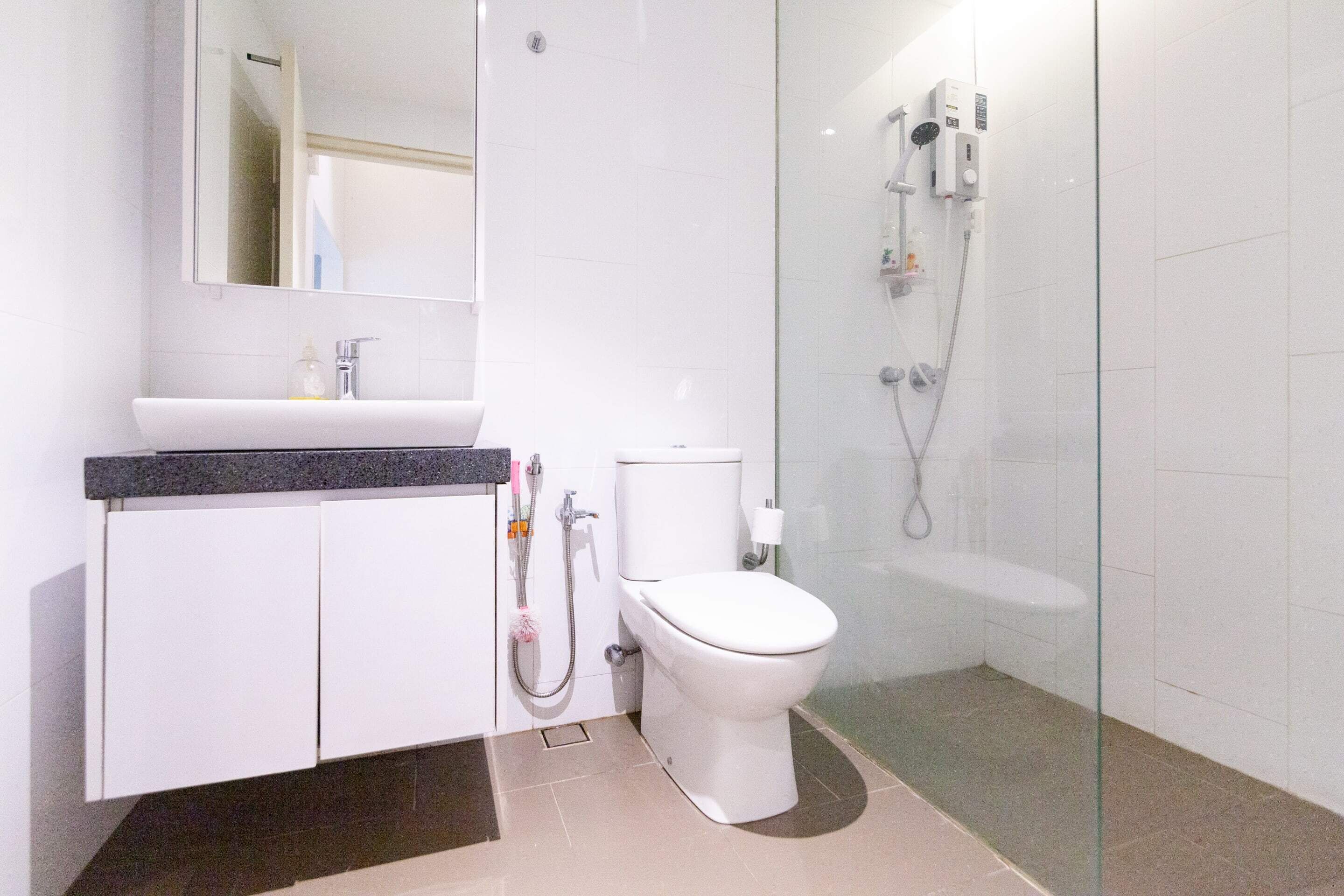 Un baño moderno con lavamanos blanco, inodoro y cabina de ducha con mampara de vidrio.