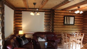 A log cabin interior with a leather sofa, a coffee table, wooden dining table, and chairs.