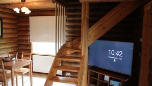 A wooden interior with a dining table, chairs, a TV displaying the time, and a staircase.
