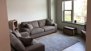 Un salon avec un canapé gris, un meuble en bois, un tapis gris et un ventilateur de plafond.