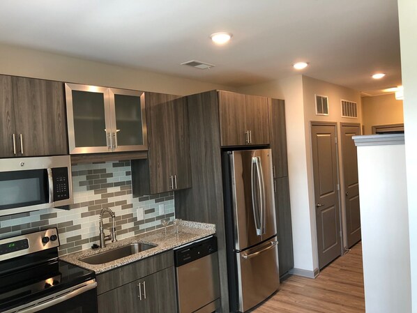 A modern kitchen with stainless steel appliances, dark wood cabinets, and a tiled backsplash.