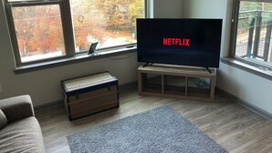 Un salon avec une grande télévision affichant le logo de Netflix, une commode en bois et un tapis gris.