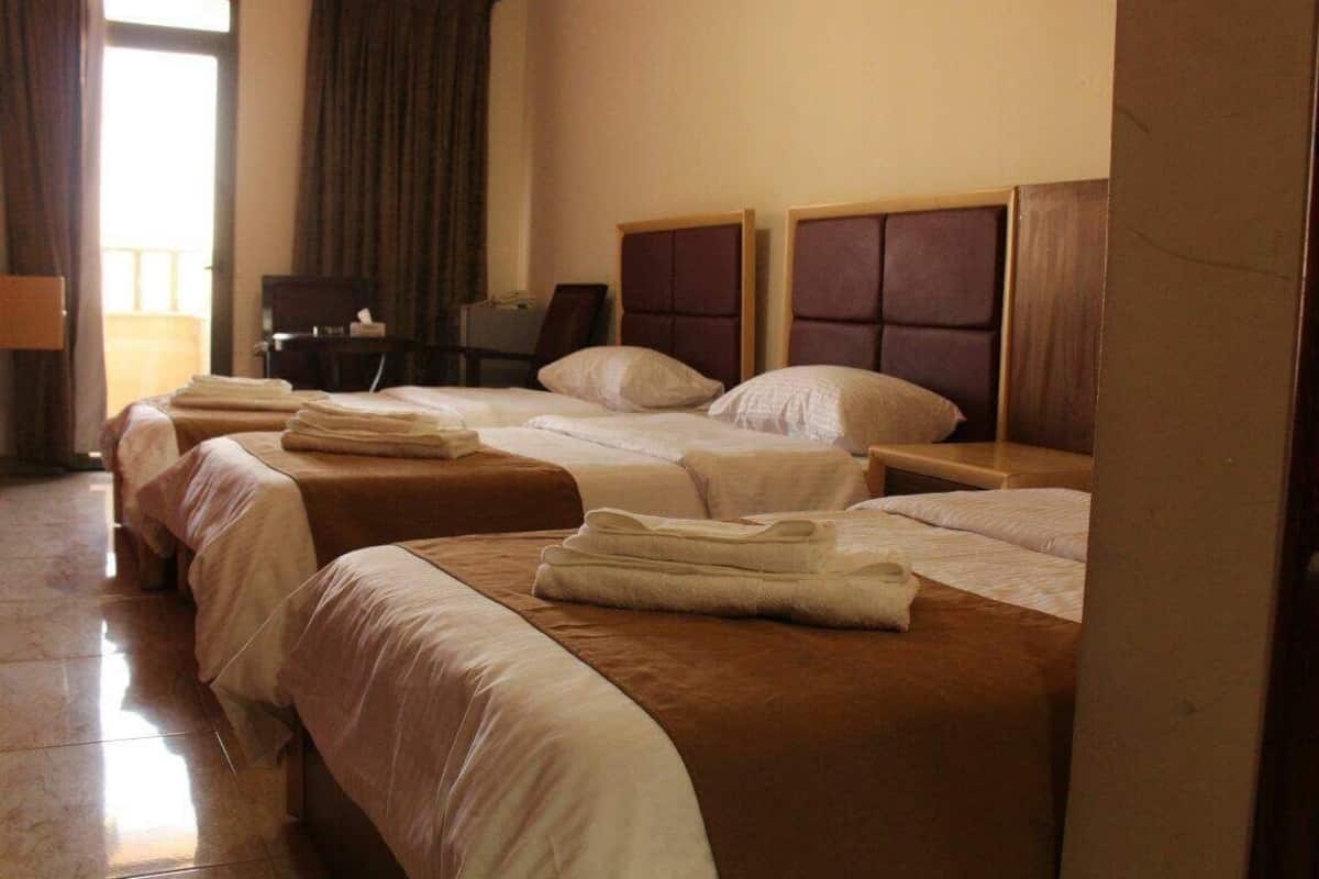 A hotel room with three beds, a desk, and a chair.