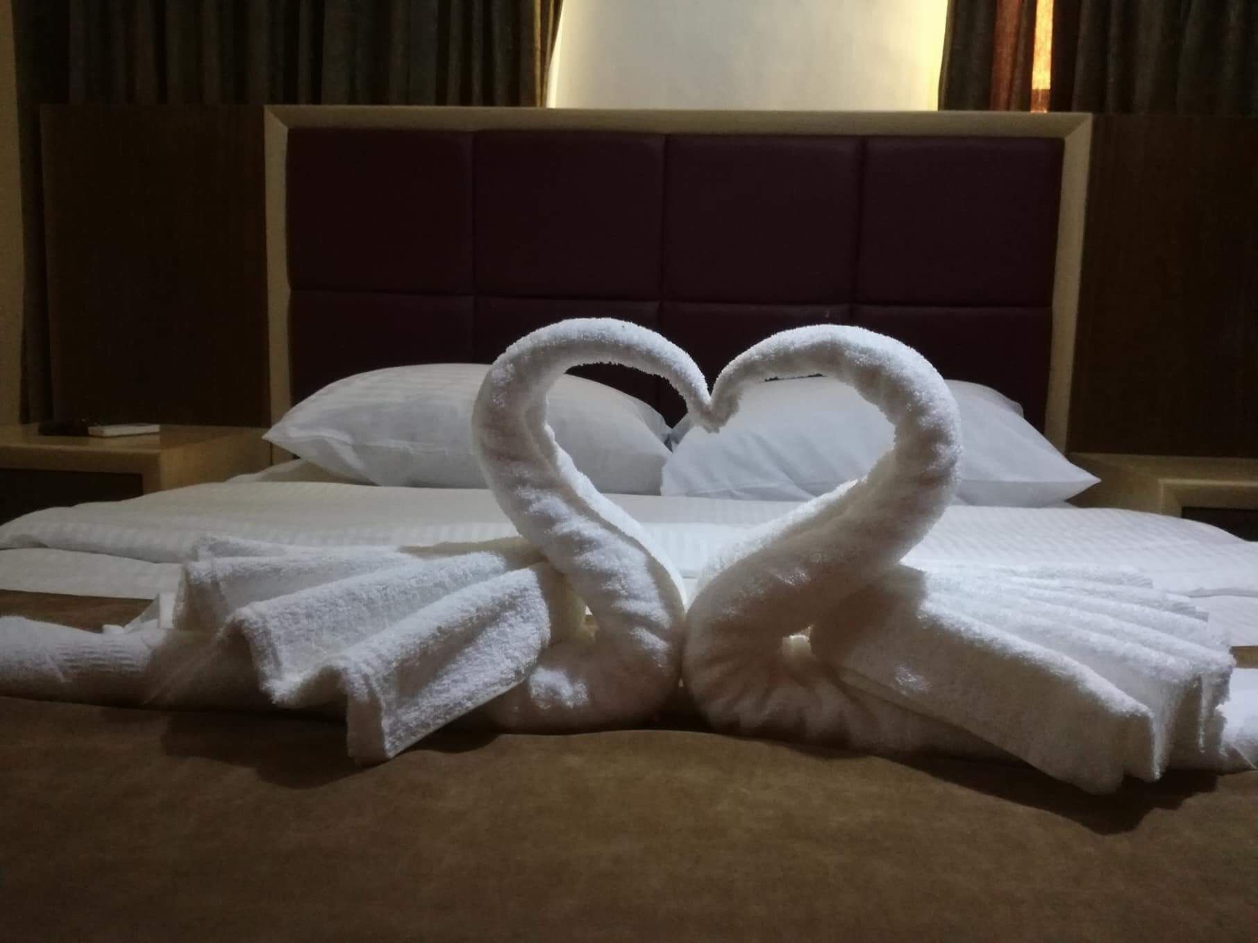A hotel room with a bed, pillows, and a decorative towel arrangement in the shape of swans.