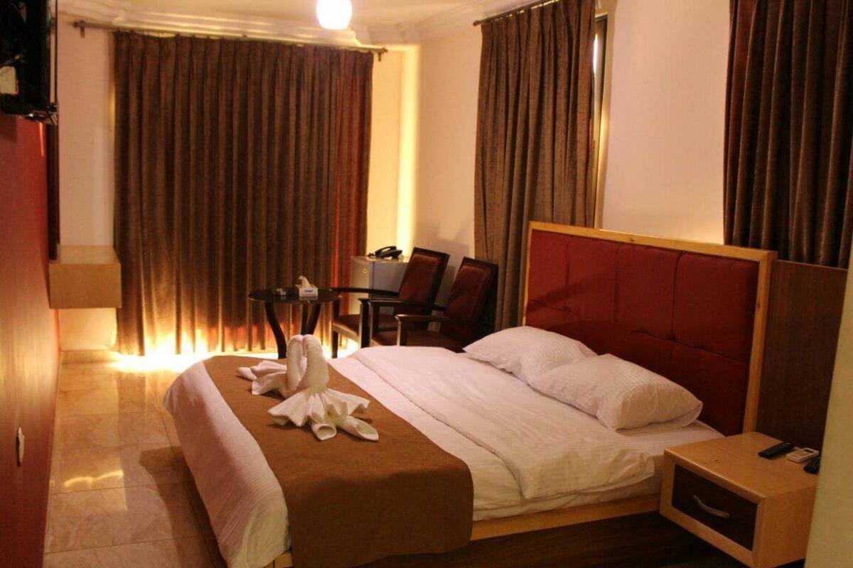 A hotel room with a bed, a bedside table, a desk with a chair, and a wardrobe.
