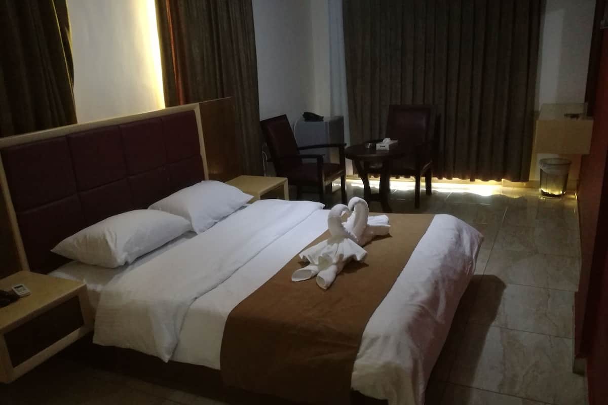 A hotel room with a bed, a desk, a chair, and a trash bin.