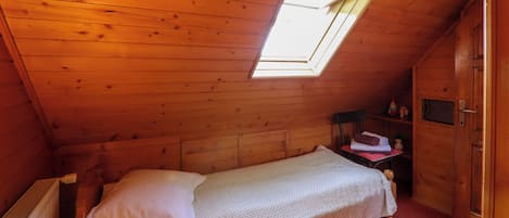 Une petite chambre avec un lit simple, un plafond en pente et un puits de lumière.