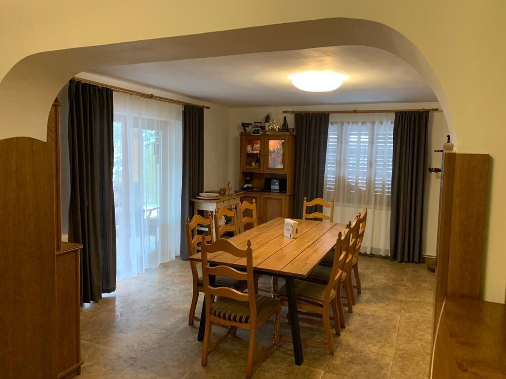 A dining area with a wooden table and chairs, a cabinet with a microwave, and a window with curtains.