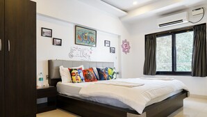 A modern bedroom with a large bed, a wardrobe, a bedside table, and a window with curtains. - Athi Resorts (Marmagao)