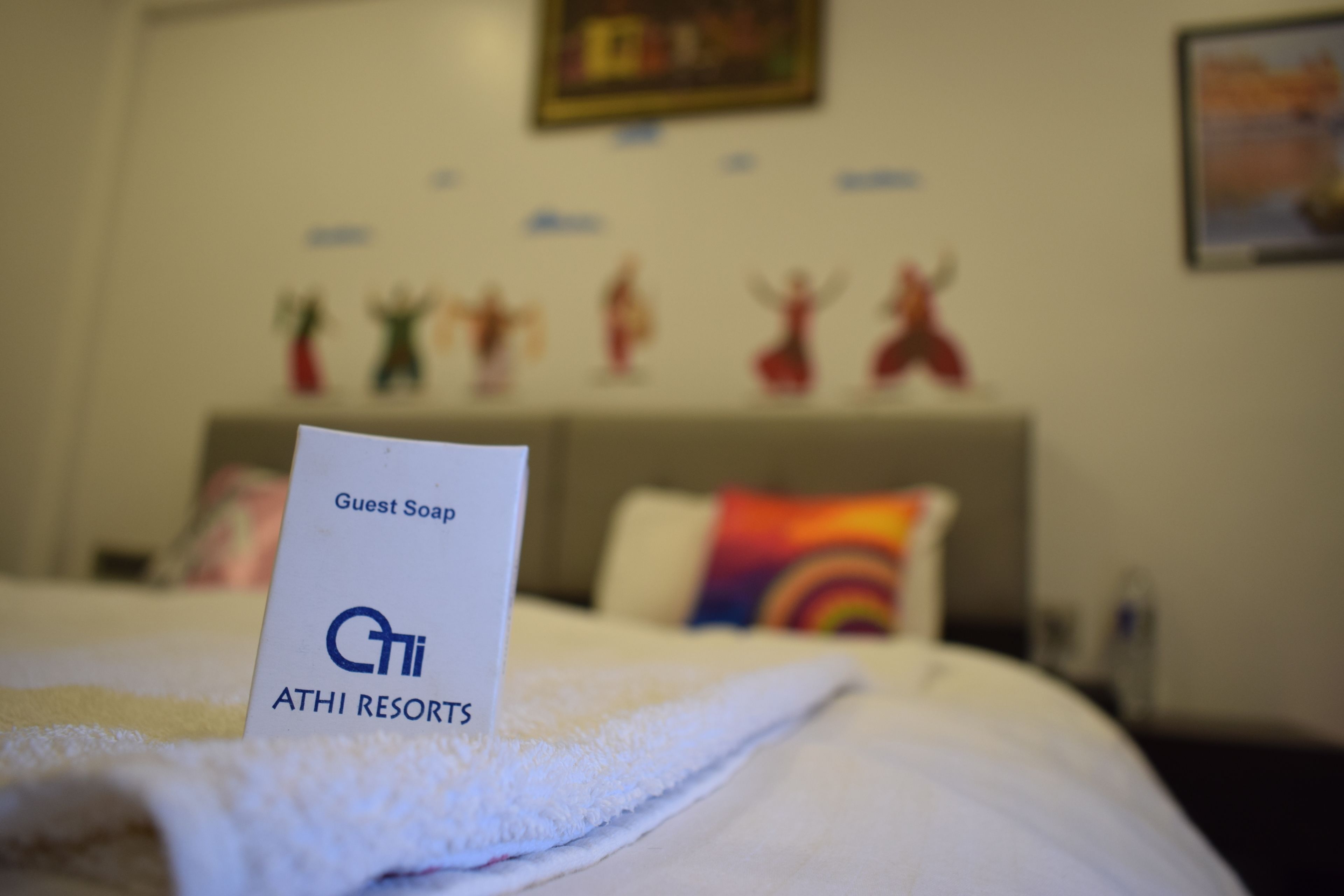 Une chambre d’hôtel avec un lit, un panneau indiquant « savon pour les clients » et « ATHI RESORTS », et un mur décoré de différents objets.