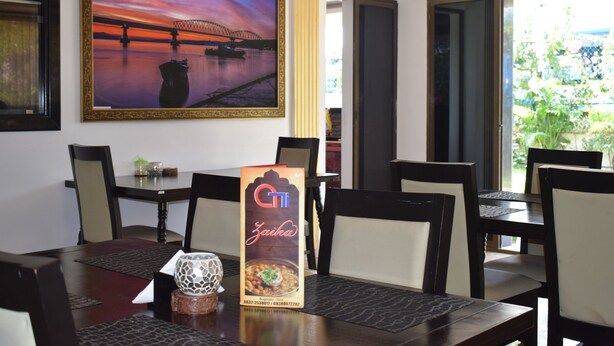 A dining area with a table set for four, a framed picture of a sunset over a bridge, and a menu stand. - Athi Resorts (Marmagao)
