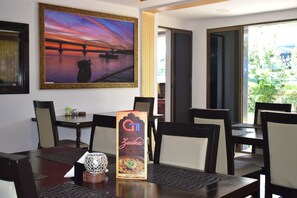 A dining area with a table set for four, a framed picture of a sunset over a bridge, and a menu stand. - Athi Resorts (Marmagao)