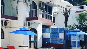 A swimming pool with blue-tiled walls, red lounge chairs, and two blue umbrellas. - Athi Resorts (Marmagao)