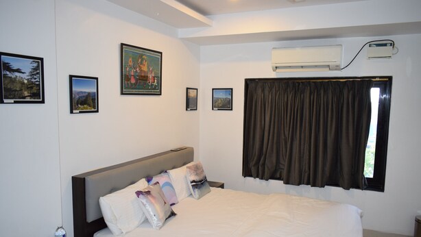 A hotel room with a large bed, a nightstand with a bottle of water, a remote control, and framed pictures on the wall. - Athi Resorts (Marmagao)