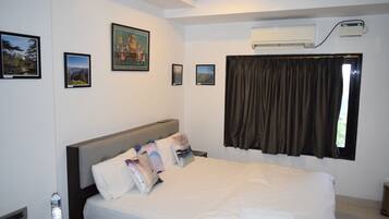 A hotel room with a large bed, a nightstand with a bottle of water, a remote control, and framed pictures on the wall.