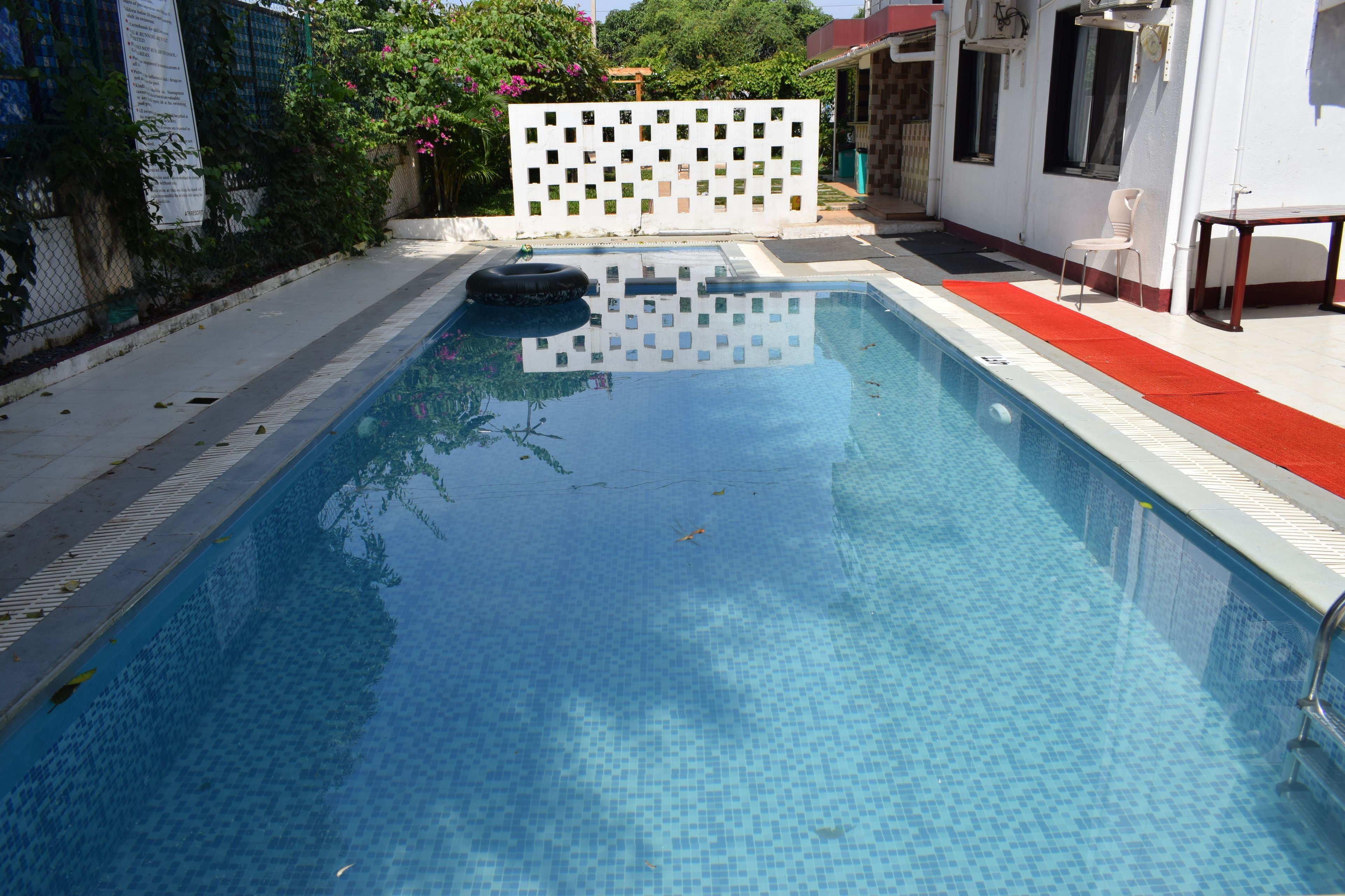 Una piscina rectangular con borde de azulejos, un flotador y una valla blanca con un diseño al fondo.