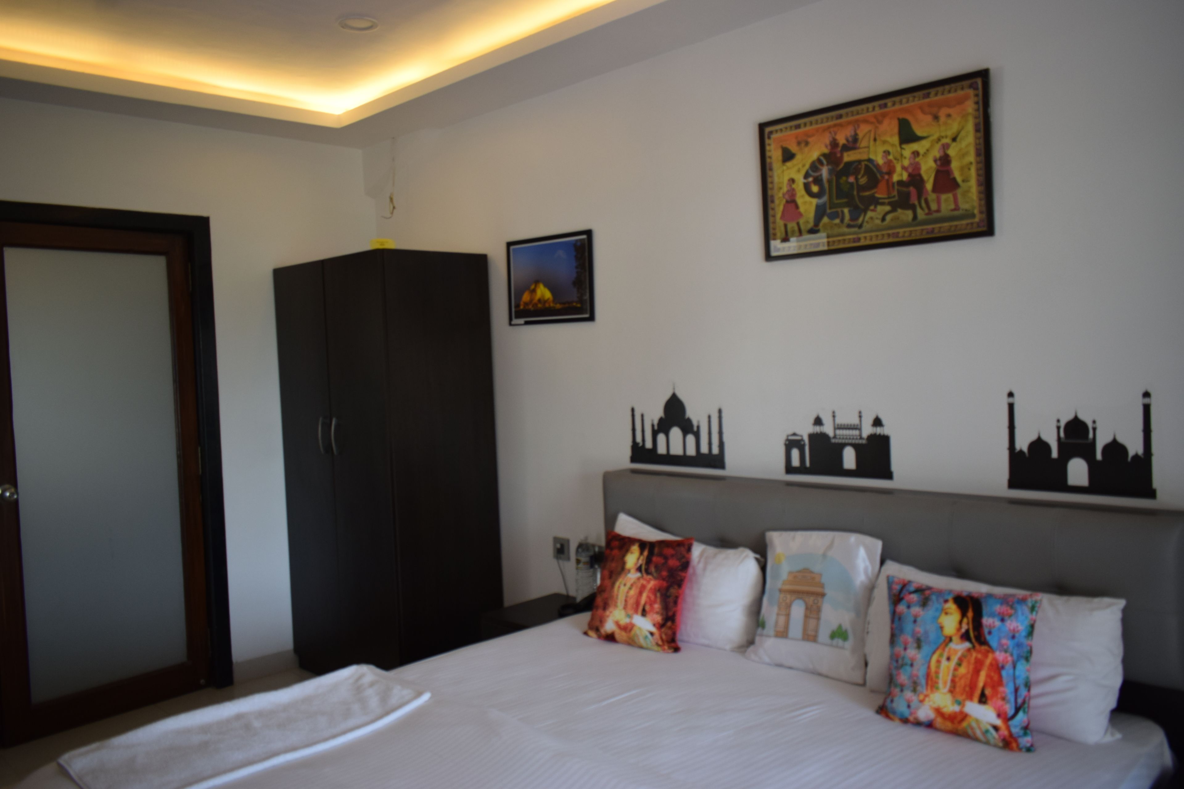 Une chambre d’hôtel comprenant un lit, une armoire et des éléments de décoration murale, notamment un tableau et des silhouettes de structures architecturales.