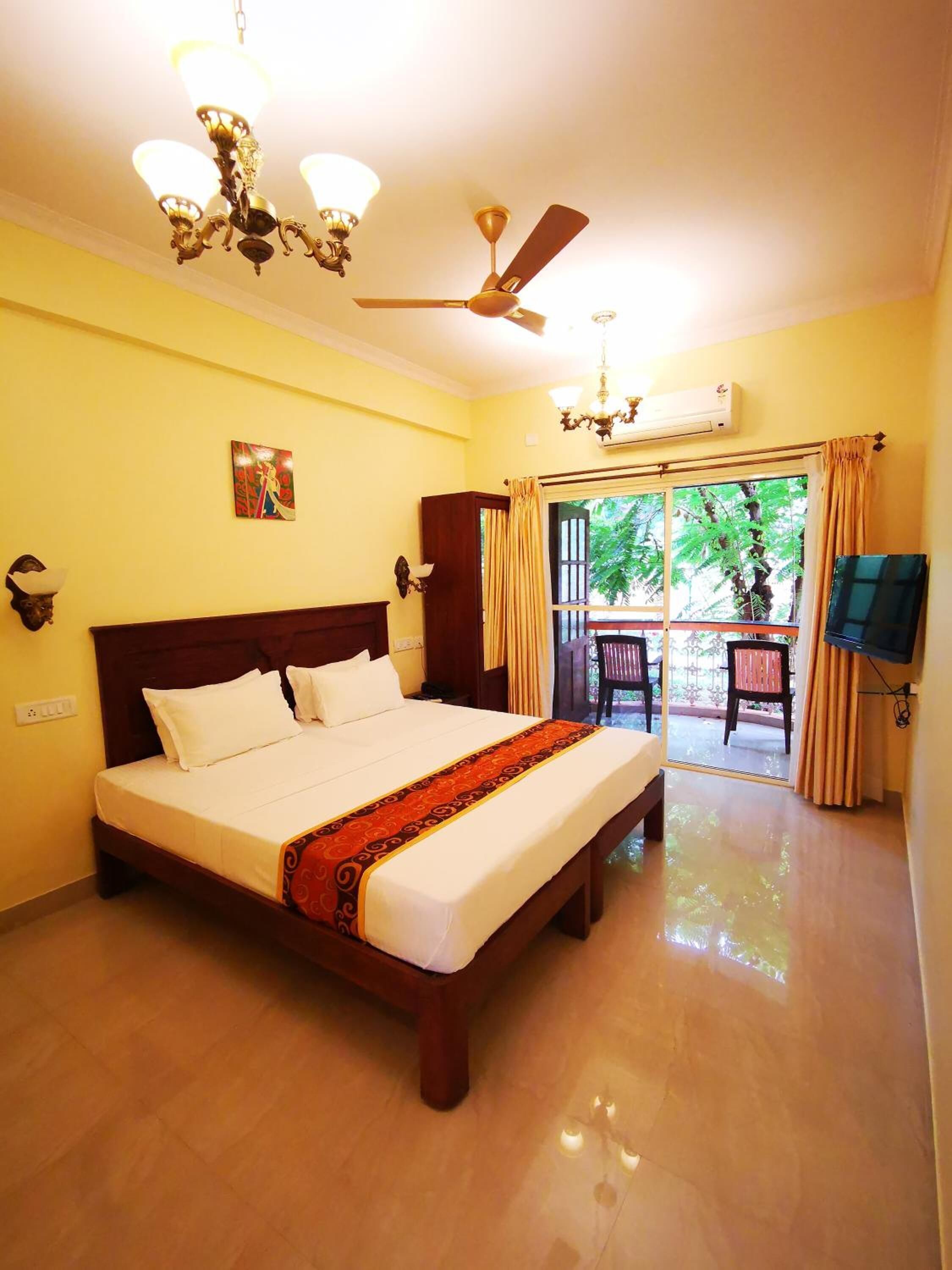 Quarto de hotel com cama grande, ventilador de teto, lustre e vista para o exterior.