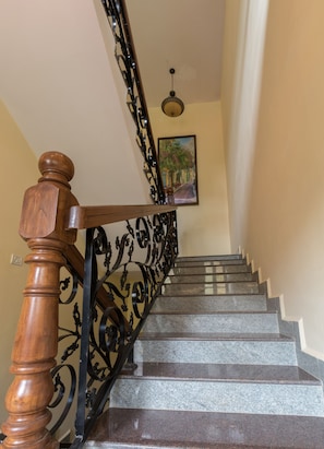 A staircase with a wooden handrail and ornate black metal balusters, leading to a room with a painting on the wall. - Resort Palmeiras Dourado (Cansaulim)