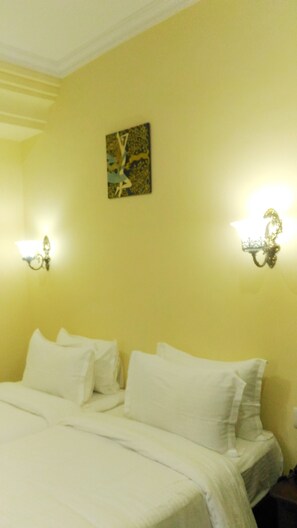 Habitación de hotel con cama, ropa de cama blanca, un cuadro en la pared y apliques.