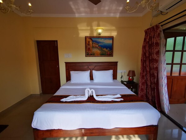 A hotel room with a large bed, a painting on the wall, a nightstand with a lamp, and a window with curtains. - Resort Palmeiras Dourado (Cansaulim)