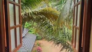 Une fenêtre ouverte donnant sur un jardin avec des palmiers et un toit recouvert de tuiles.