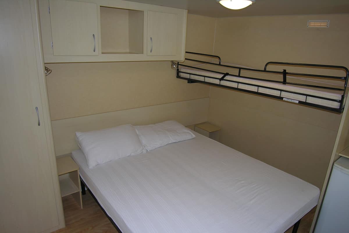 Une chambre avec un lit simple et un lit superposé au-dessus, une petite table de chevet et un placard au-dessus du lit.