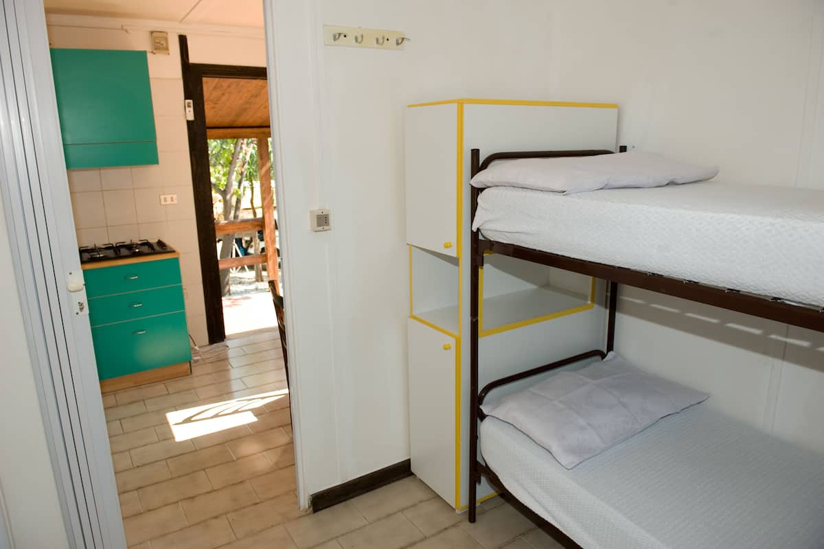 Un lit superposé avec un matelas blanc et une structure jaune, une armoire turquoise et un espace cuisine bien visible avec une cuisinière.
