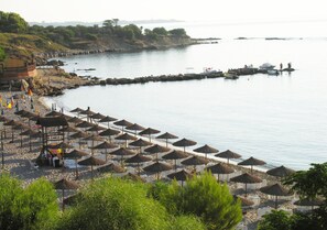 Uma praia com fileiras de guarda-sóis de palha e uma orla rochosa.