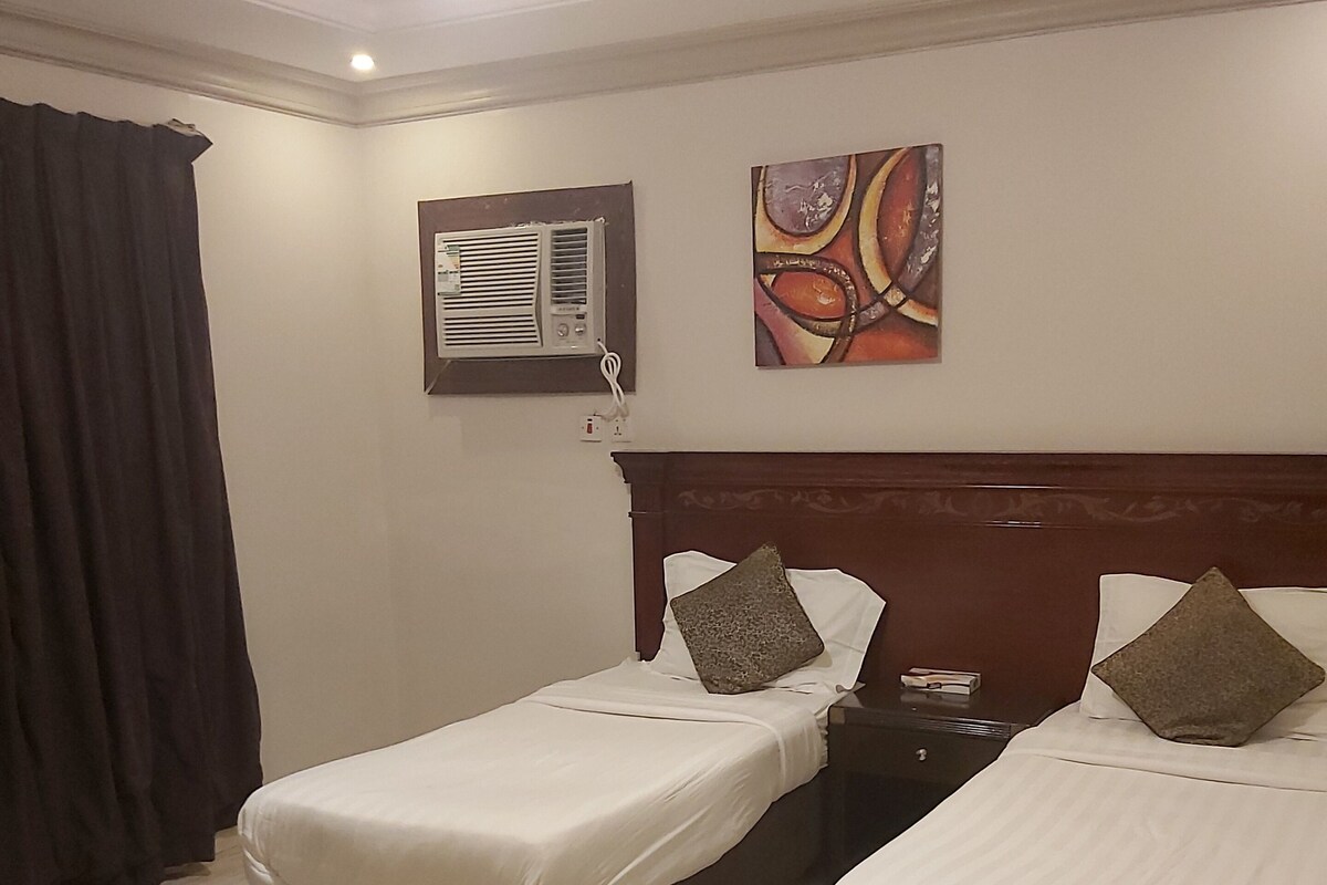 Une chambre d’hôtel avec deux lits, une table de chevet, un climatiseur fixé au mur et un tableau.
