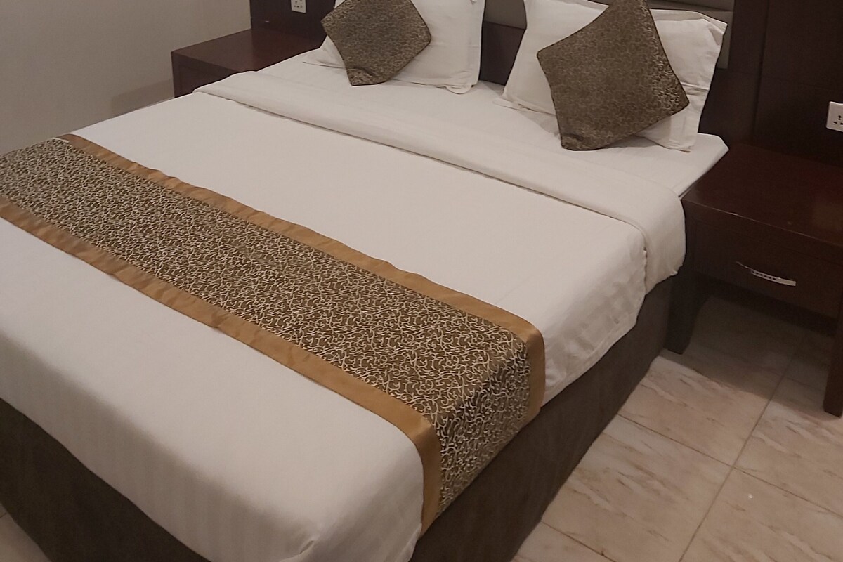 Un lit bien fait, avec une couvre-lit à motifs, deux oreillers et une tête de lit.
