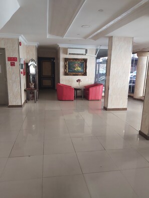 Un hall d’entrée spacieux avec un sol ciré, une horloge comtoise, des sièges rouges et une œuvre d’art encadrée accrochée au mur.