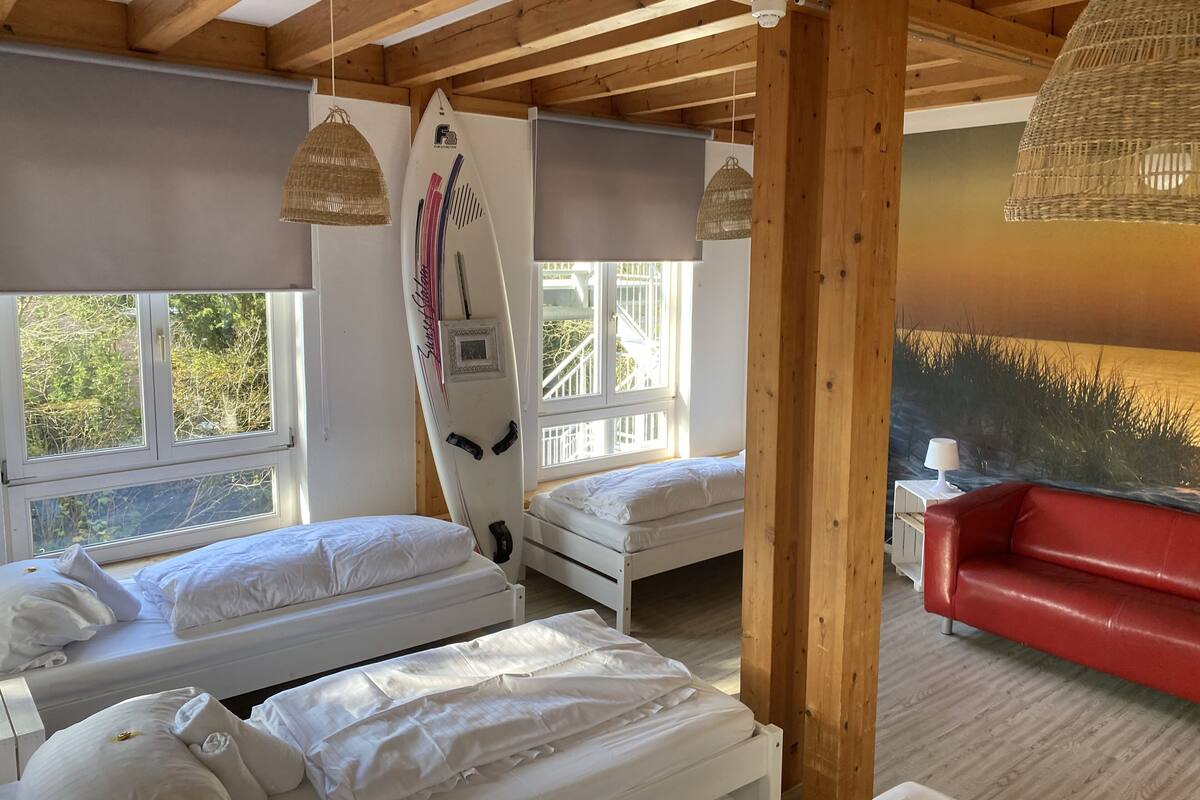 A room with wooden beams, two beds, a red couch, and a surfboard decoration.