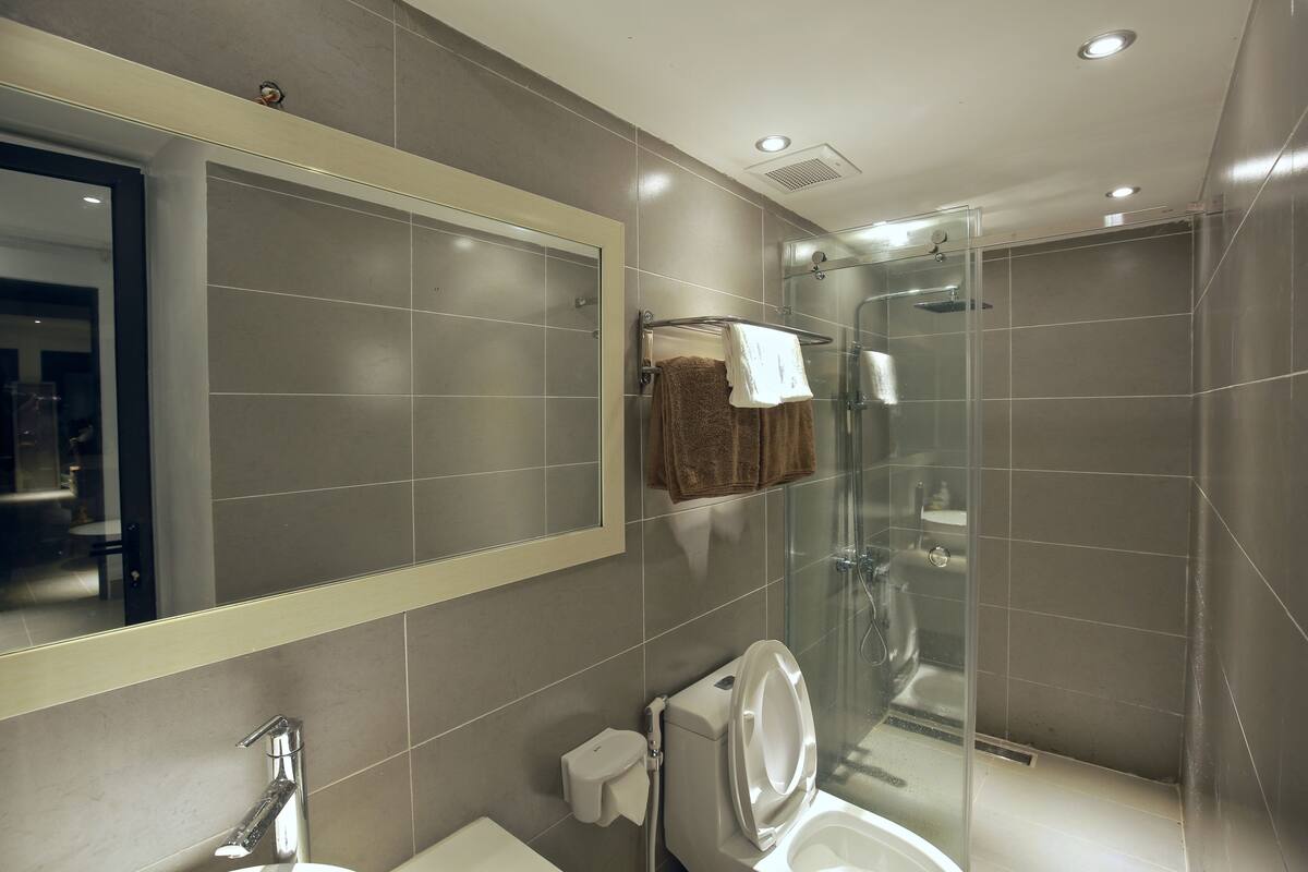 A modern bathroom with a large mirror, a toilet, a sink, and a glass-enclosed shower area.