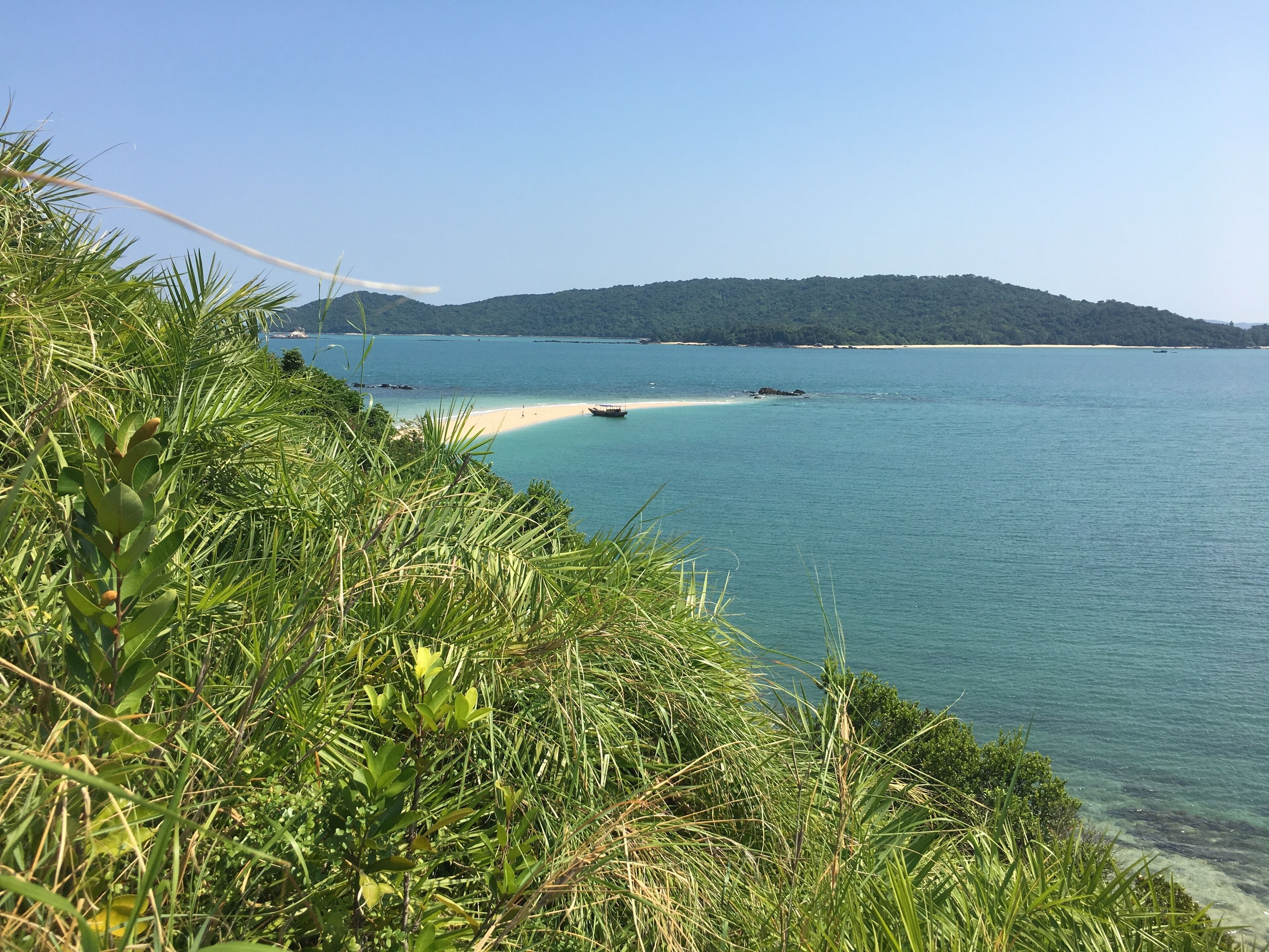 A coastal landscape with a sandy beach, clear blue water, and lush greenery.