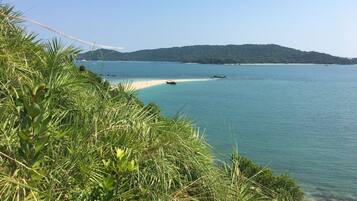 A coastal landscape with a sandy beach, clear blue water, and lush greenery.