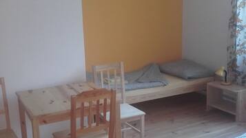 A room with a wooden floor, a bed with a checkered bedspread, a small table with chairs, and a wall with a yellow section.