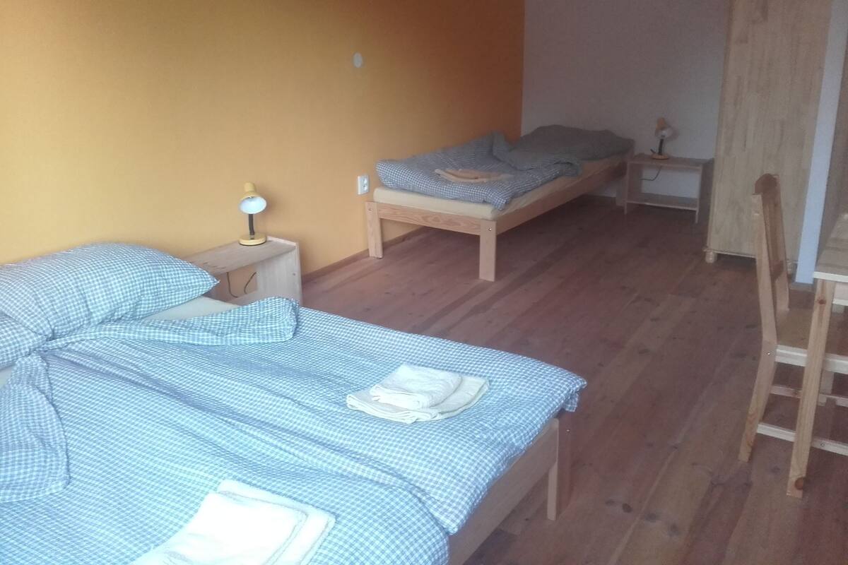 A small, single-room accommodation with two beds, a desk, and a chair.