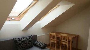 A small, cozy room with a sloped ceiling and skylights, a gray sofa with patterned cushions, and a wooden table. - Kyprův mlýn (Knínice)